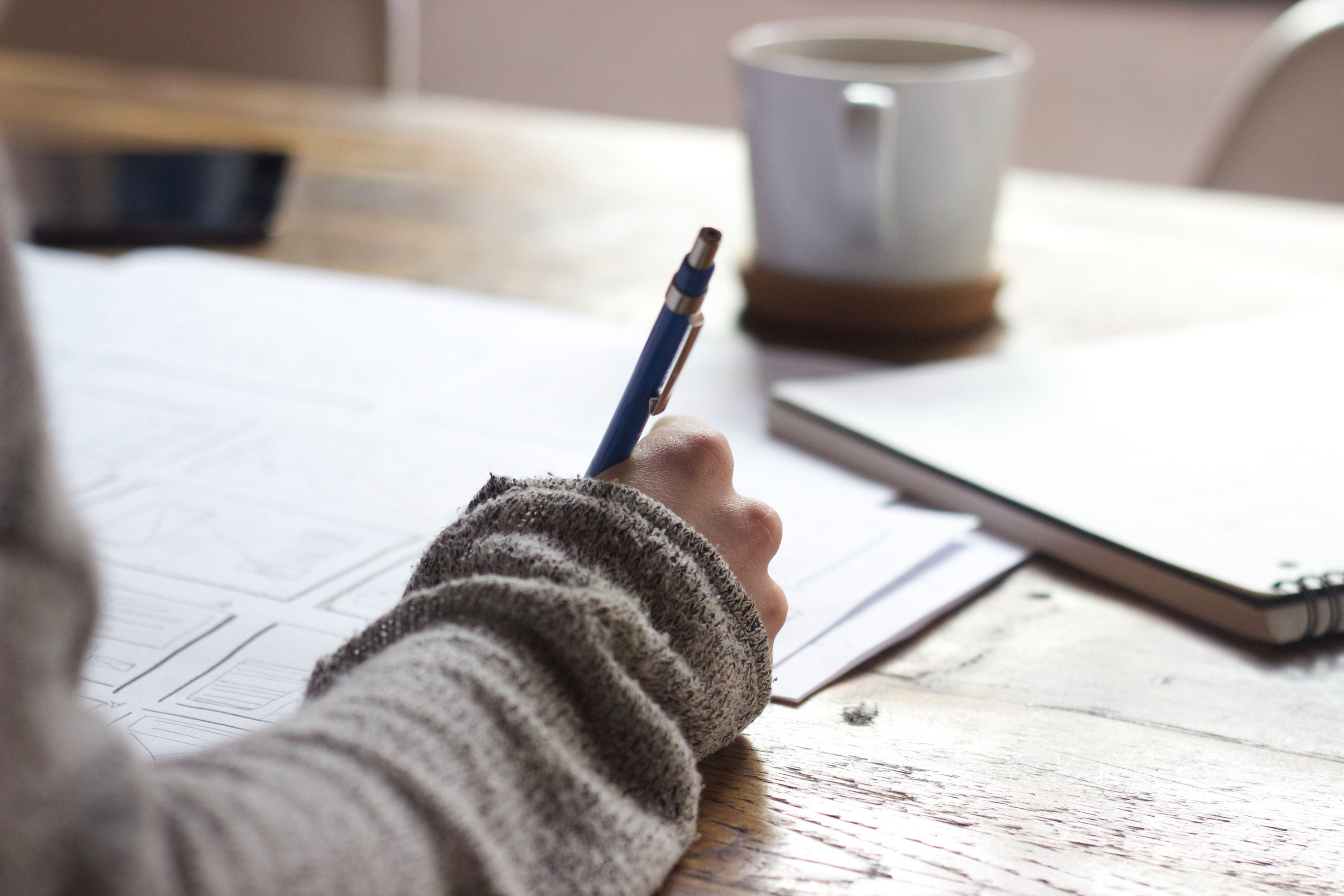 Person writing on paper with a pen at a desk